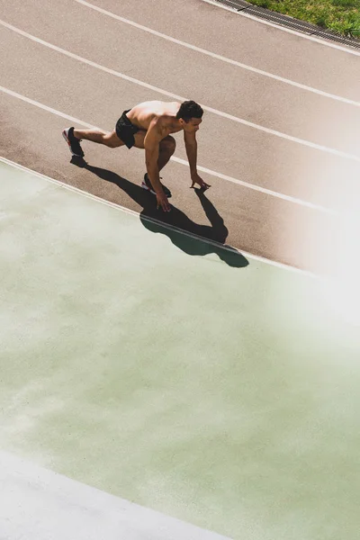 Overhead view of mixed race sportsman preparing to run at stadium — Stock Photo