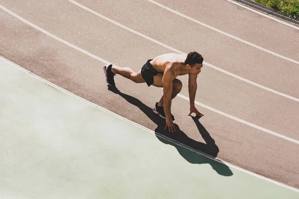 Overhead view of mixed race sportsman preparing to run at stadium — Stock Photo