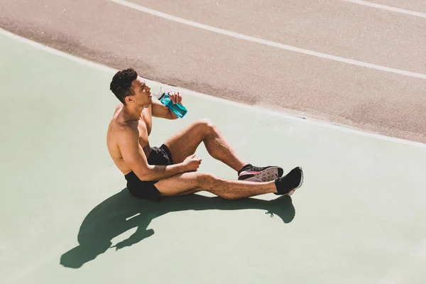 Mixed race sportsman sitting at stadium and drinking water — Stock Photo