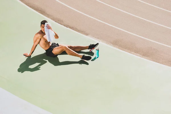 Deportista de carrera mixta sentado en el estadio y limpiando la cara con una toalla - foto de stock