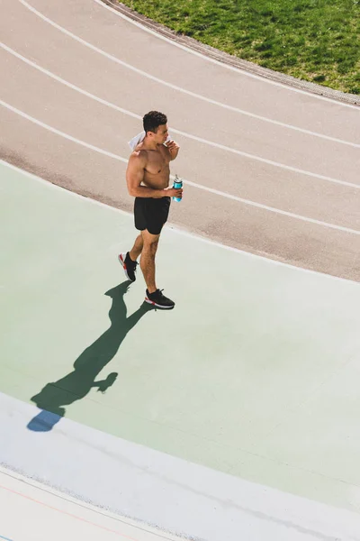 Вид сверху на смешанную гонку спортсмен держит полотенце и спортивную бутылку на стадионе — стоковое фото