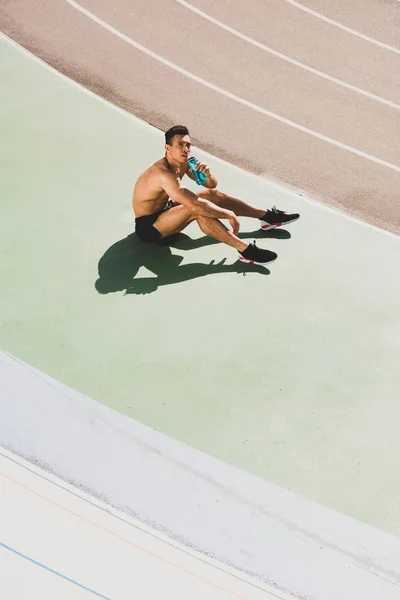 Mixed race sportsman sitting at stadium and drinking water — Stock Photo