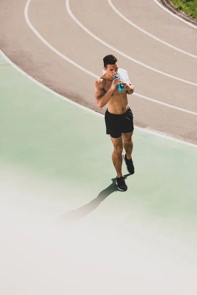 Vista completa del deportista de carrera mixta sosteniendo la toalla y la botella de deporte en el estadio - foto de stock