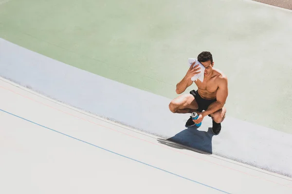 Overhead view of mixed race sportsman sitting at stadium and wiping face with towel — Stock Photo