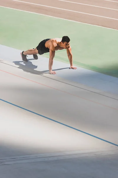 Mixed race sportsman standing in plank at stadium — Stock Photo