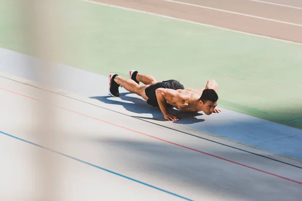 Shirtless mixed race sportsman doing push ups at stadium — Stock Photo