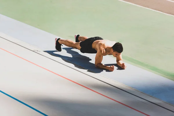 Mixed race sportsman standing in plank at stadium — Stock Photo