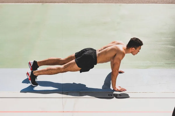 Mixed race sportsman standing in plank at stadium — Stock Photo