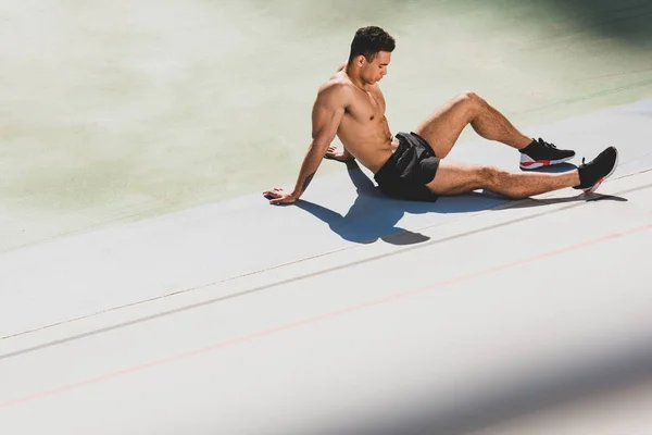 Tired handsome mixed race sportsman sitting at stadium — Stock Photo