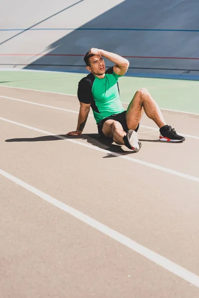 Cansado deportista de carrera mixta sentado en el estadio y tocando la  cabeza — Correr, relajante - Stock Photo | #270350444