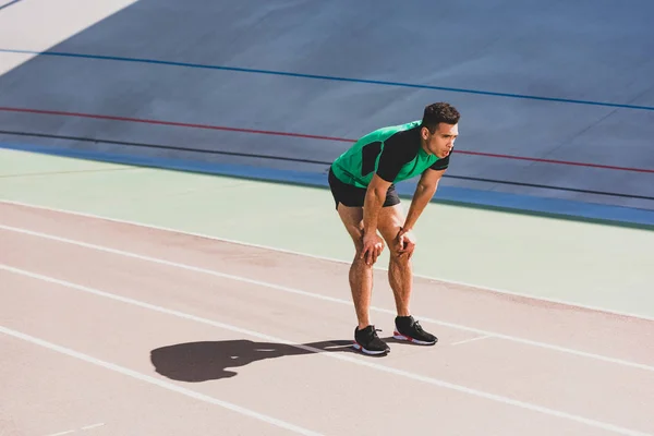 Уставший смешанный спортсмен в спортивной одежде, стоящий на стадионе с руками на коленях — стоковое фото