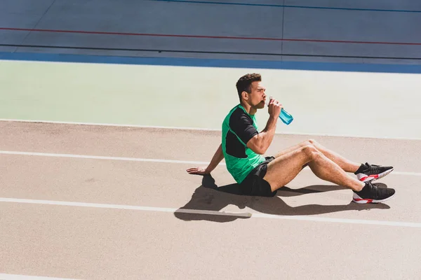 Mixed race sportsman sitting at stadium and drinking water — Stock Photo
