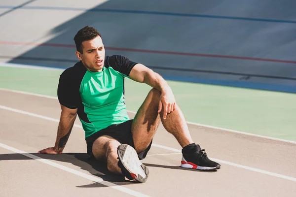 Tired handsome mixed race sportsman sitting at stadium — Stock Photo