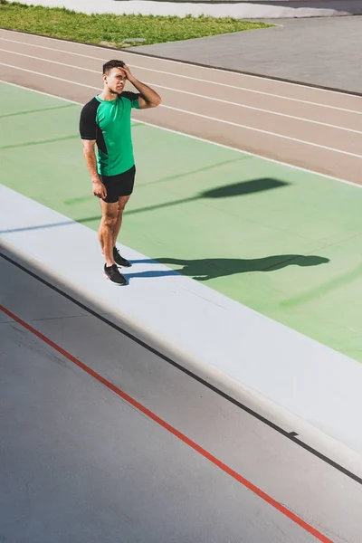 Vista a tutta lunghezza di stanco atleta di razza mista in piedi allo stadio — Foto stock