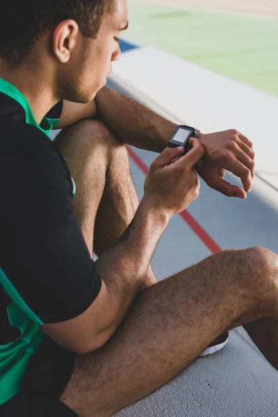 Vista recortada del deportista de carrera mixta usando smartwatch en el estadio - foto de stock