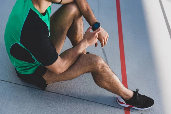 Vista cortada de desportista de raça mista usando smartwatch na pista de corrida — Fotografia de Stock