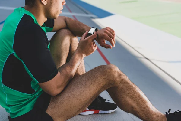 Cropped view of sportsman using smartwatch at running track — Stock Photo