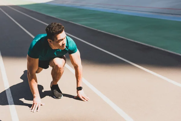 Mixed race sportsman on start position looking away at stadium — Stock Photo