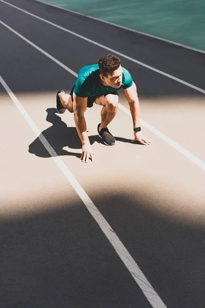 Apuesto deportista de carrera mixta en posición de inicio mirando hacia otro lado en el estadio - foto de stock