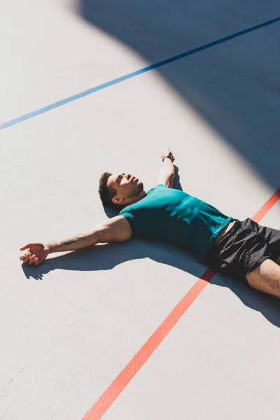 Mixed race sportsman laying on running track and spread arms — Stock Photo