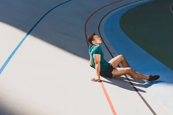 Vue latérale du sportif mixte assis sur la piste de course au stade par temps ensoleillé — Photo de stock