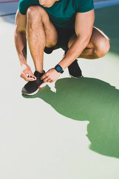 Cropped view of sportsman lacing up sneakers at stadium — Stock Photo