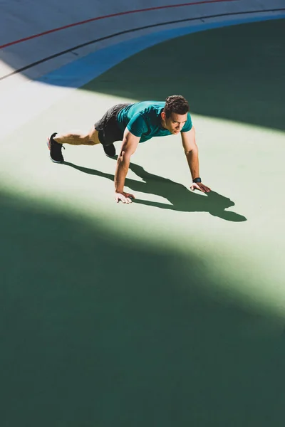 Mixed race sportsman pressing up at stadium — Stock Photo