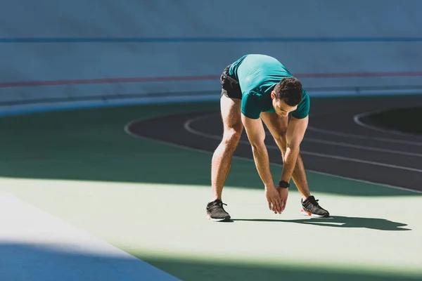 Mixed race sportsman stretching at stadium, standing in sunlight on green floor — Stock Photo