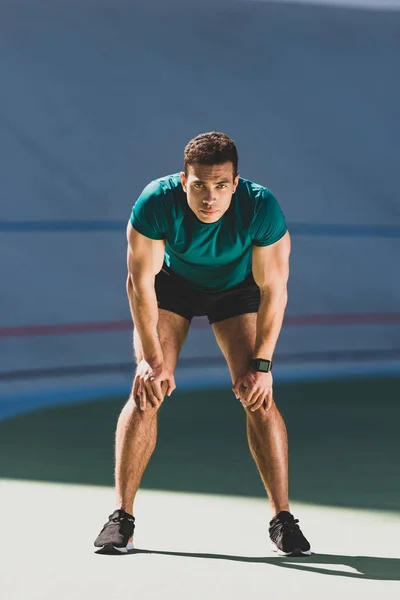 Frontansicht eines Mixed-Race-Sportlers mit Händen auf Knien, der im Stadion an einem hellen Ort steht — Stockfoto