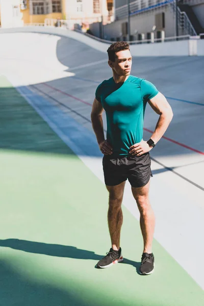 Sportif de course mixte musclé debout avec les mains sur les hanches au stade à la lumière du soleil — Photo de stock