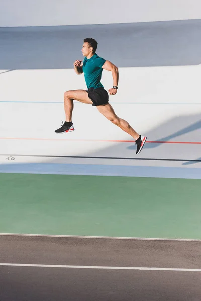 Vista lateral de la carrera muscular mixta deportista sprint corriendo en el estadio - foto de stock