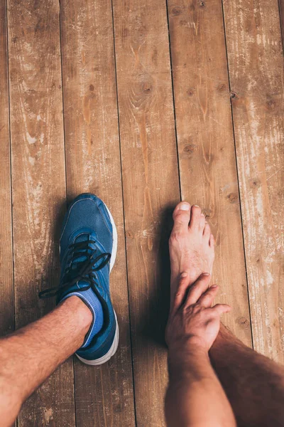 Vista parziale dello sportivo seduto in una scarpa da ginnastica e toccare la gamba ferita — Foto stock