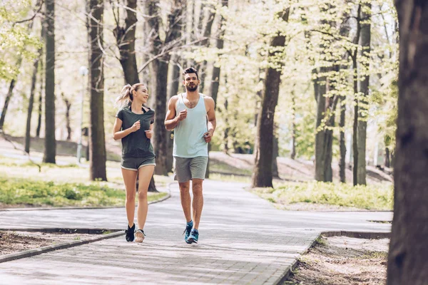 Schöner Mann und hübsche Frau lächeln beim Laufen im grünen, sonnigen Park — Stockfoto