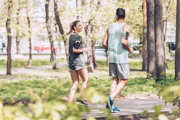 Young man and woman talking while jogging together in sunny park — Stock Photo