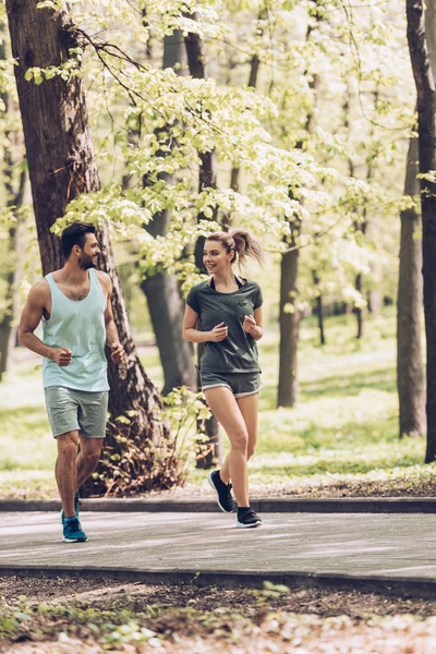 Handsome man and pretty woman in sportswear talking while running in park — Stock Photo