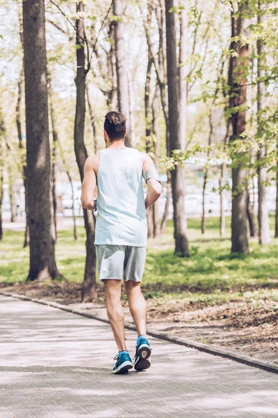 Вид сзади на молодого человека в спортивной одежде, бегущего по дорожке в парке — стоковое фото
