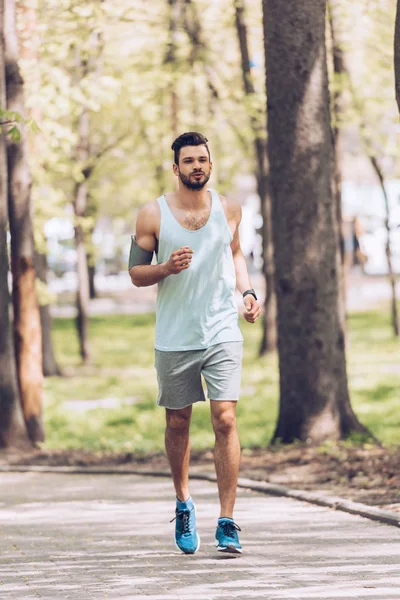 Hombre guapo en ropa deportiva corriendo por el pavimento en el parque verde - foto de stock