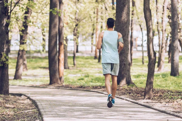 Vue arrière du jeune sportif faisant du jogging le long de la promenade dans le parc — Photo de stock