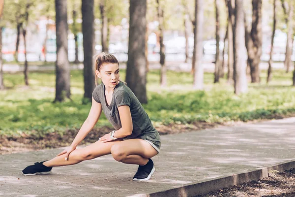 Приваблива молода жінка в спортивному одязі дивиться в сторону під час фізичних вправ в сонячному парку — стокове фото