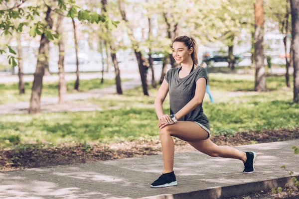 Sonriente joven deportista mirando hacia otro lado mientras hace ejercicio en el soleado parque - foto de stock