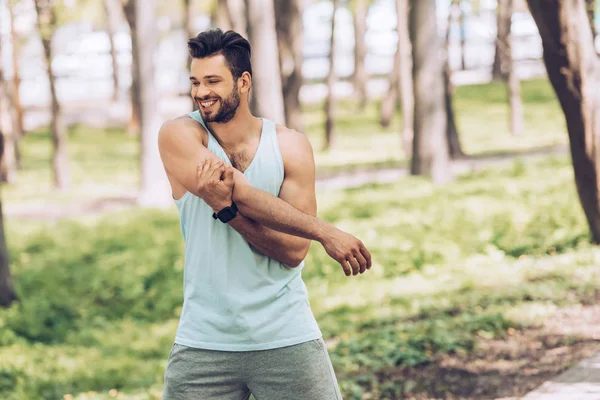 Alegre joven deportista sonriendo mientras se estira en el soleado parque - foto de stock