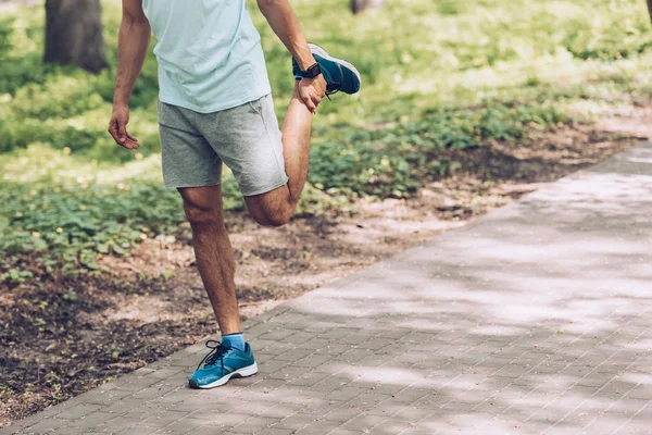 Tiro recortado del hombre en ropa deportiva y zapatillas de deporte que se extiende en el parque - foto de stock