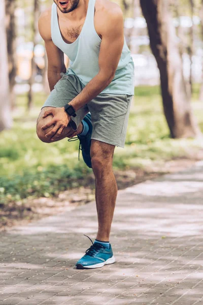 Tiro cortado de esportista tocando joelho ferido enquanto estava em pé no parque — Fotografia de Stock