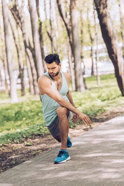 Hombre guapo en ropa deportiva haciendo ejercicio y estirándose en el parque verde - foto de stock
