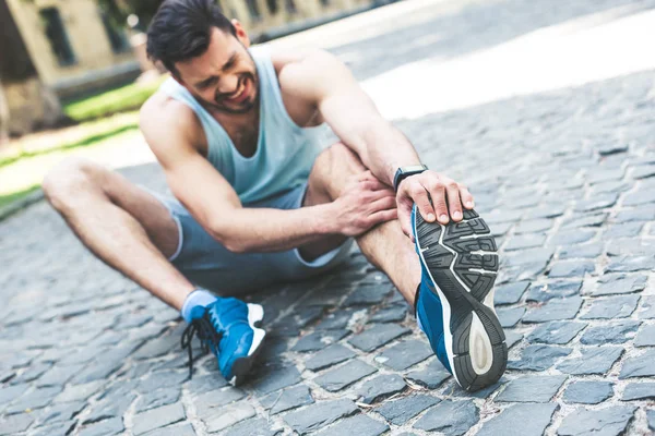Selective focus of injured sportsman sitting on pavement and touching leg — Stock Photo