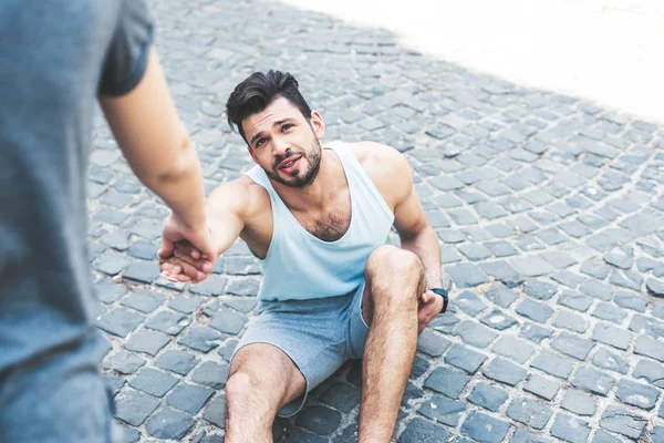 Cropped shot of woman helping injured sportsman sitting on pavement — Stock Photo