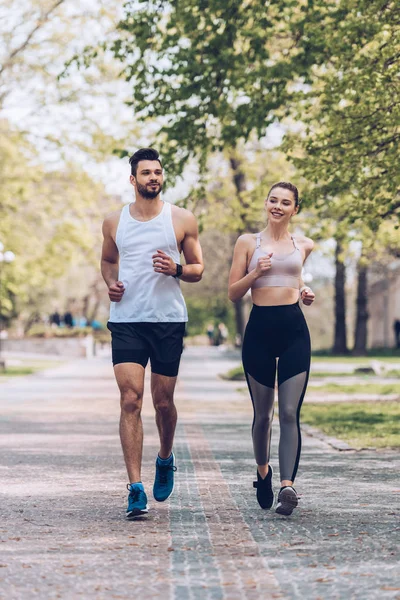 Deportista sonriente y deportista corriendo por amplio callejón en el parque - foto de stock