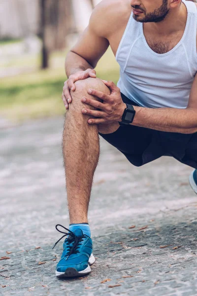 Cropped shot of man in sportswear touching injured knee — Stock Photo