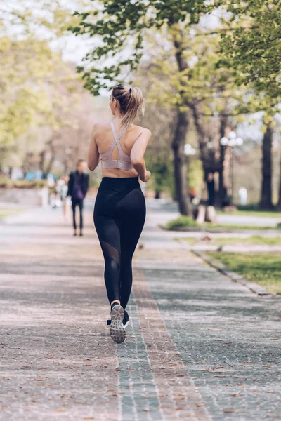 Rückansicht junge Sportlerin joggt auf breitem Gehweg im Park — Stockfoto