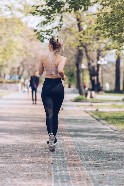 Back view of young sportswoman jogging along wide walkway in park — Stock Photo